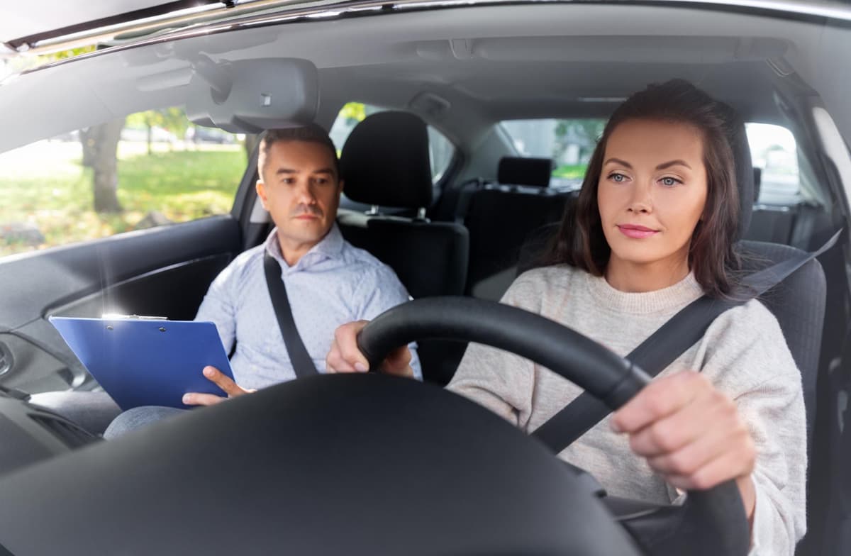 A learner driver gripping the steering wheel of a right-hand-drive car, concentrating, with her instructor beside her
